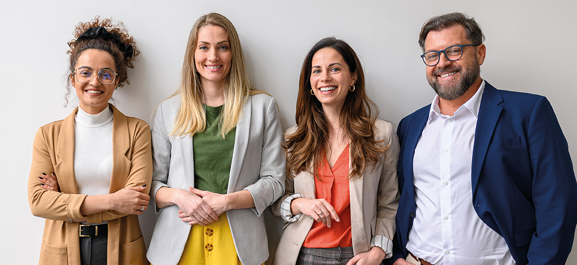 Drei Damen und ein Herr stehen in einer Reihe dem Betrachter zugewandt.